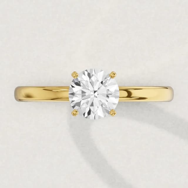 Face-up view of a yellow gold four-claw solitaire engagement ring on a 2 mm band with a 1 carat round diamond 6.5 mm across, a 3D render drawn to the same scale as the other face-up rings on this page