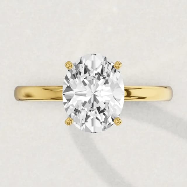 Face-up view of a yellow gold four-claw solitaire engagement ring on a 2 mm band with an oval diamond the size of our 2 carat ovals, about 10.3 by 7.2 mm, running along the finger, a 3D render drawn to the same scale as the other face-up rings on this page