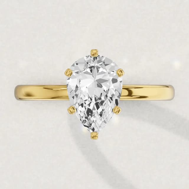 Face-up view of a yellow gold claw-set solitaire engagement ring on a 2 mm band with a pear diamond the size of our 2 carat pears, about 11.4 by 7.1 mm, point towards the fingertip, a 3D render drawn to the same scale as the other face-up rings on this page