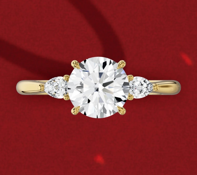 Three-stone engagement ring with a round centre diamond and two pear side stones pointing outwards, in yellow gold, by Lily Dia Jewellery