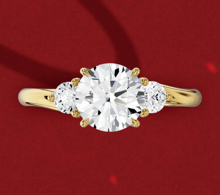 Three-stone engagement ring with a round centre diamond and two round side stones in yellow gold, seen from above, by Lily Dia Jewellery