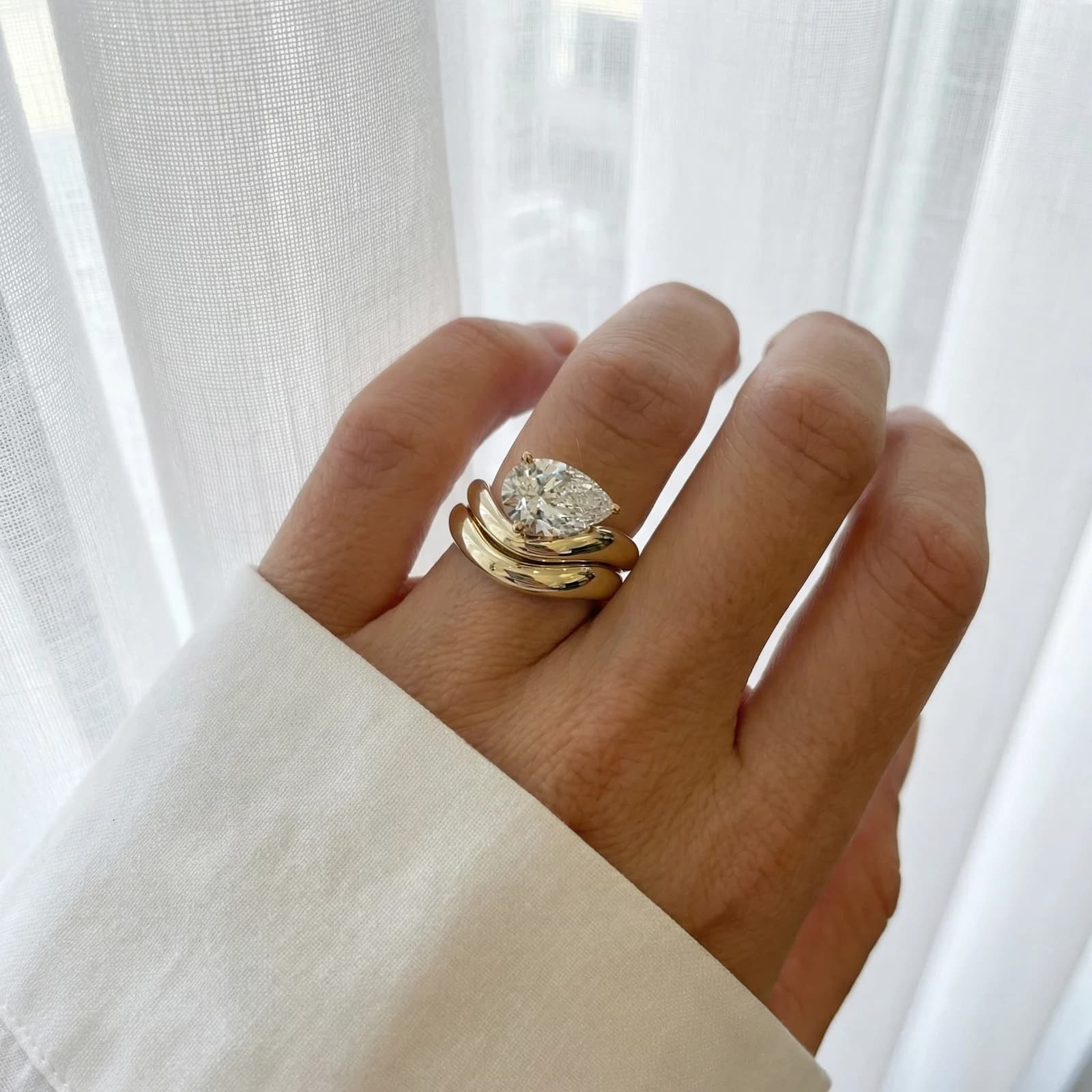 A pear shaped diamond engagement ring with a wrapped wedding band worn on the hand, a pear shaped diamond shape education guide by Lily Dia Jewellery