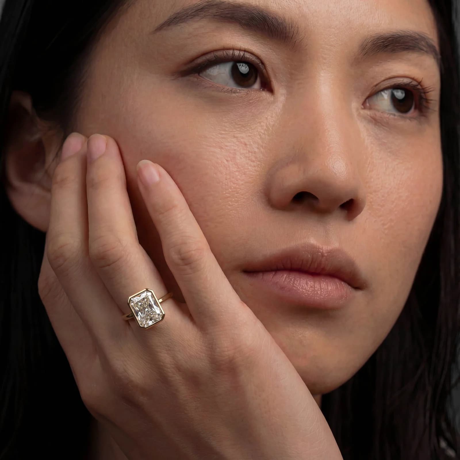A model wearing a radiant cut lab-grown diamond bezel set engagement ring in yellow gold, a radiant cut diamond shape education guide by Lily Dia Jewellery