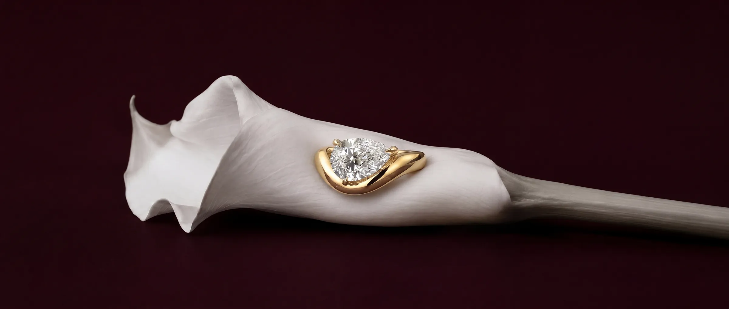 A gold engagement ring set with a lab-grown diamond or moissanite, resting in a white calla lily
