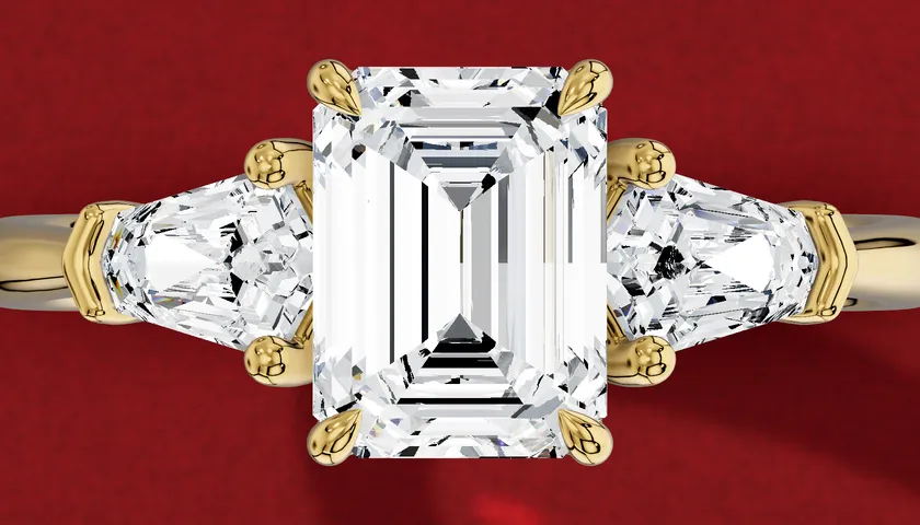 3D render seen from above of a yellow gold ring with an emerald-cut centre diamond between two shield-shaped side diamonds.