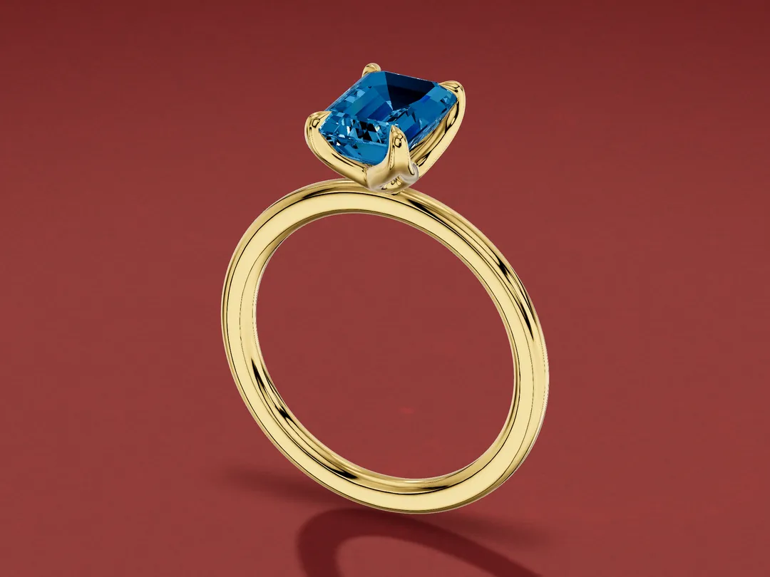 3D render of an emerald-cut deep steely blue London blue topaz in a four-claw yellow gold solitaire ring.