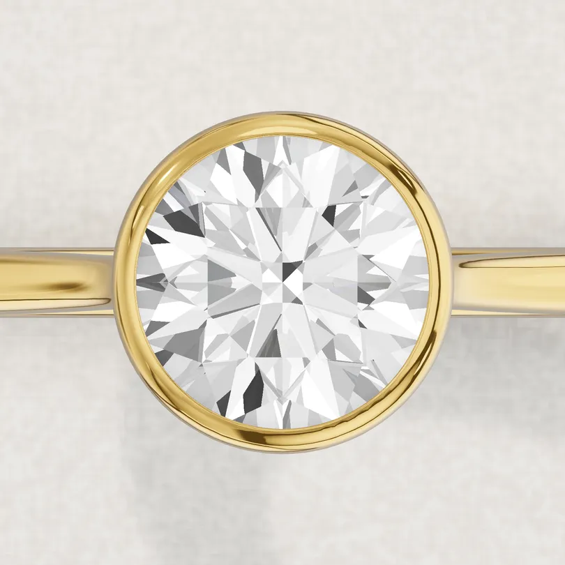 3D render of a 1 carat round diamond in a yellow gold bezel, a rim of metal around the whole stone, seen from above