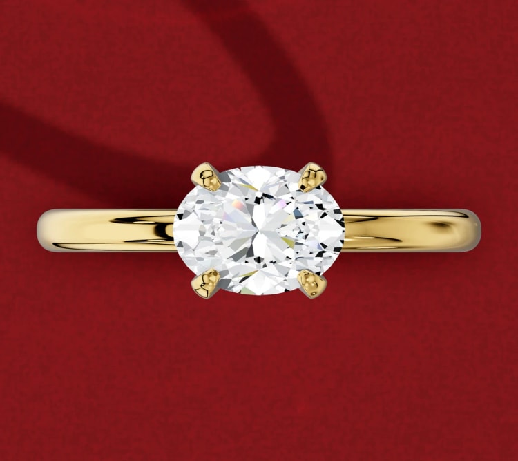 East-west oval diamond engagement ring with four claws, the oval set sideways across a plain yellow gold band, by Lily Dia Jewellery