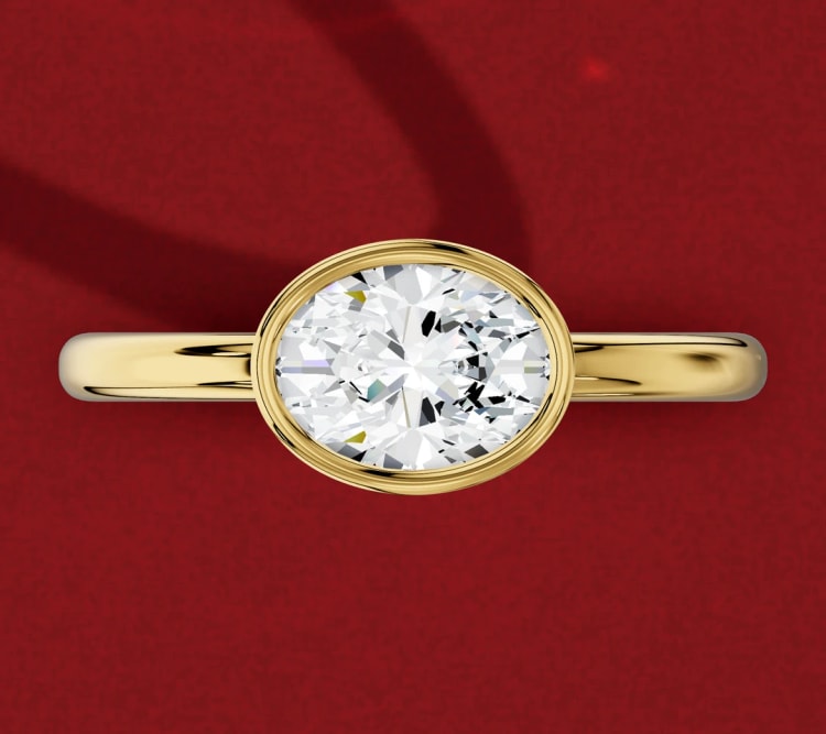 East-west oval diamond in a yellow gold bezel setting, set sideways across a plain band, by Lily Dia Jewellery