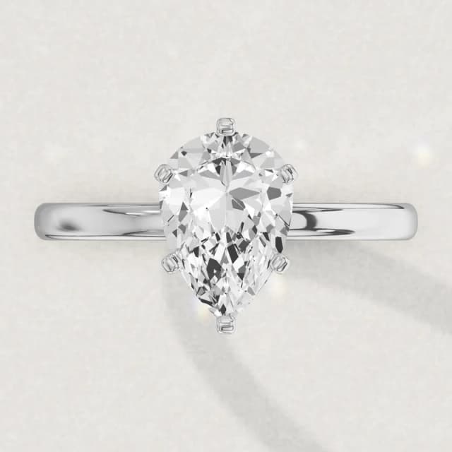 Face-up view of a white gold claw-set solitaire engagement ring on a 2 mm band with a pear diamond the size of our 2 carat pears, with a claw over its point, a 3D render drawn to the same scale as the other face-up rings on this page
