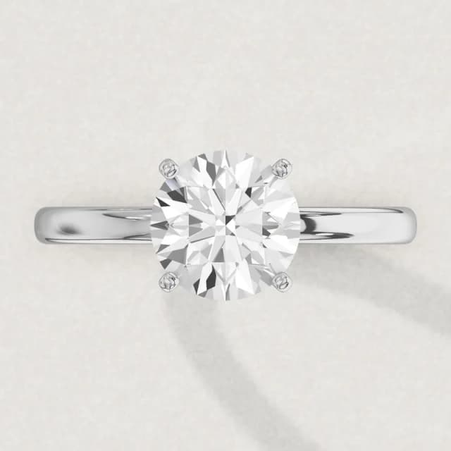 Face-up view of a white gold four-claw solitaire engagement ring on a 2 mm band with a 2 carat round diamond 8.1 mm across, a 3D render drawn to the same scale as the other face-up rings on this page