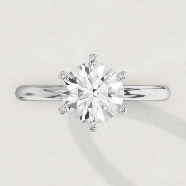 Face-up view of a white gold six-claw solitaire engagement ring on a 2 mm band with a 2 carat round diamond 8.1 mm across, a 3D render drawn to the same scale as the other face-up rings on this page