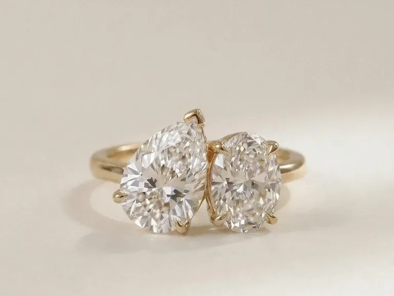 Photo of a toi et moi ring with a pear-shaped and an oval diamond set next to each other on a yellow gold band.