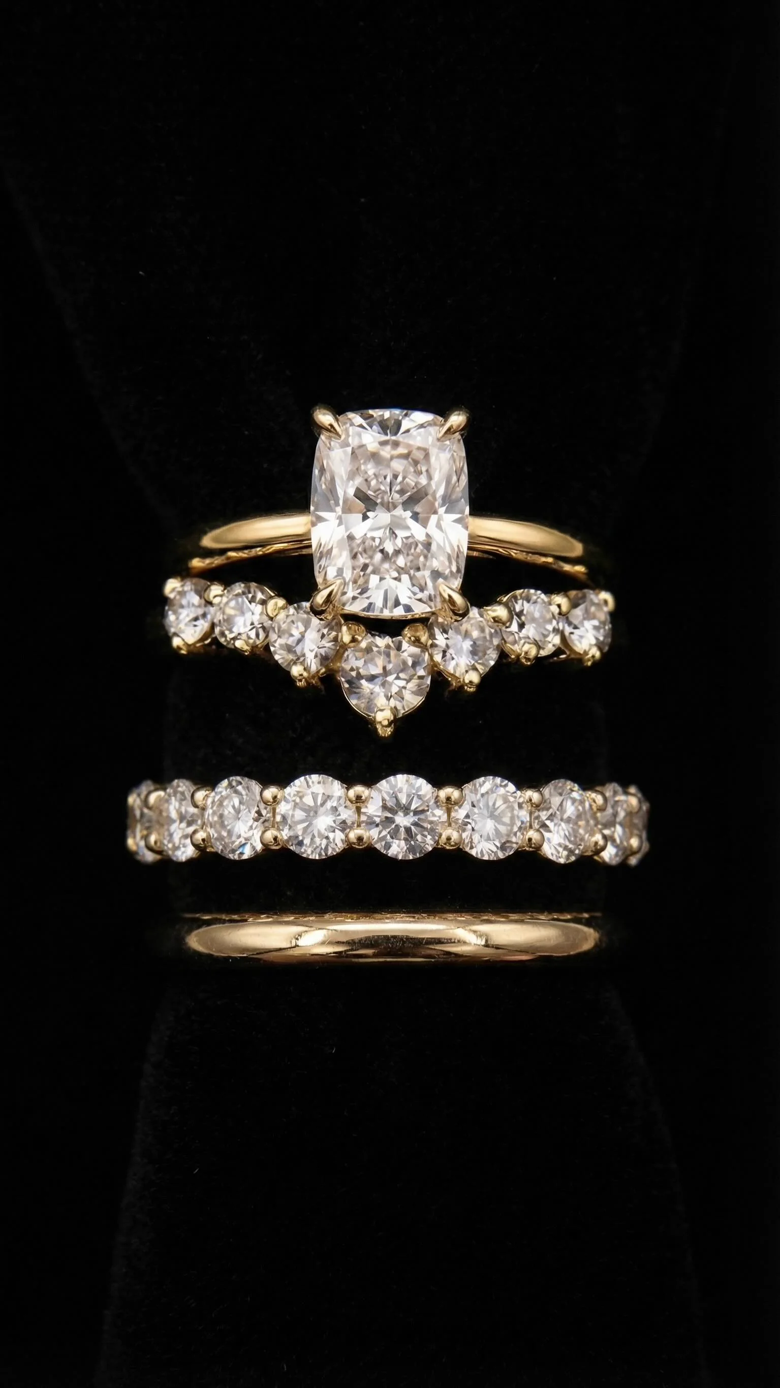 Cushion-cut diamond engagement ring with two diamond wedding bands on black velvet