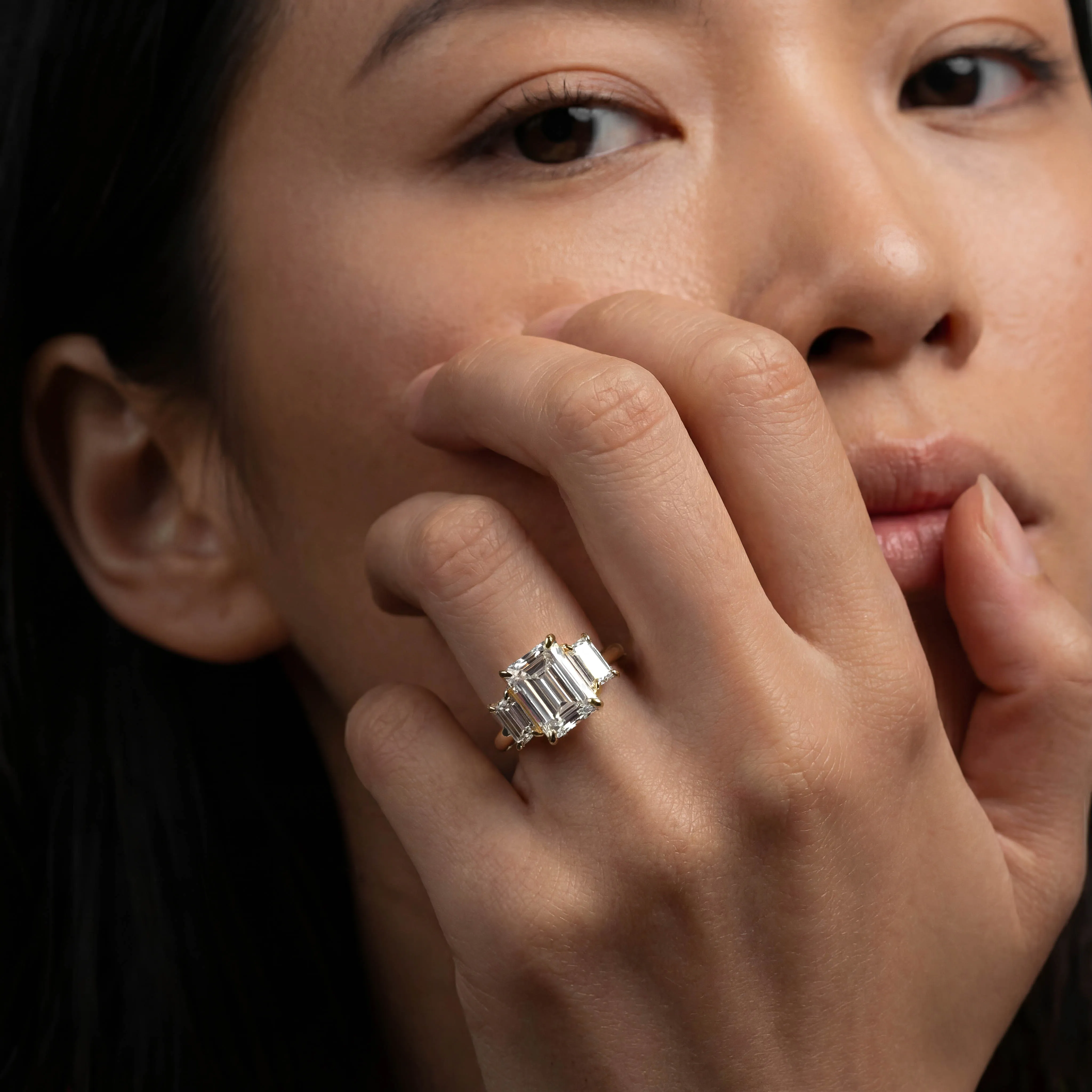 Emerald cut three stone lab-grown diamond engagement ring in yellow gold worn on the hand