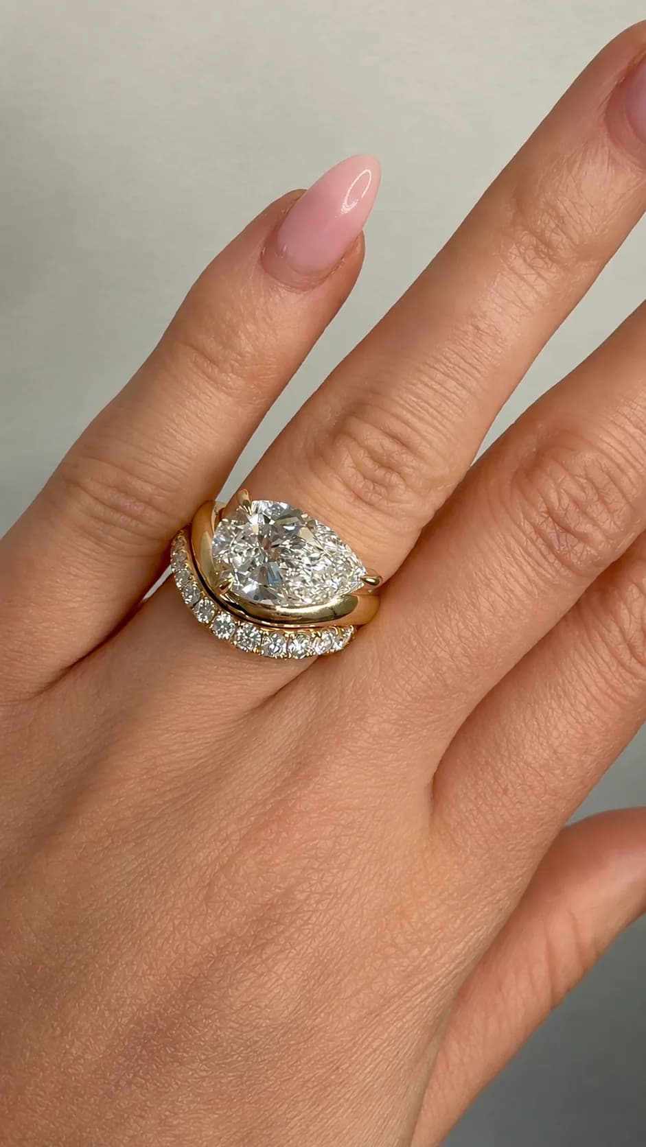 Pear cut lab-grown diamond engagement ring in yellow gold, worn with a curved pave wedding band